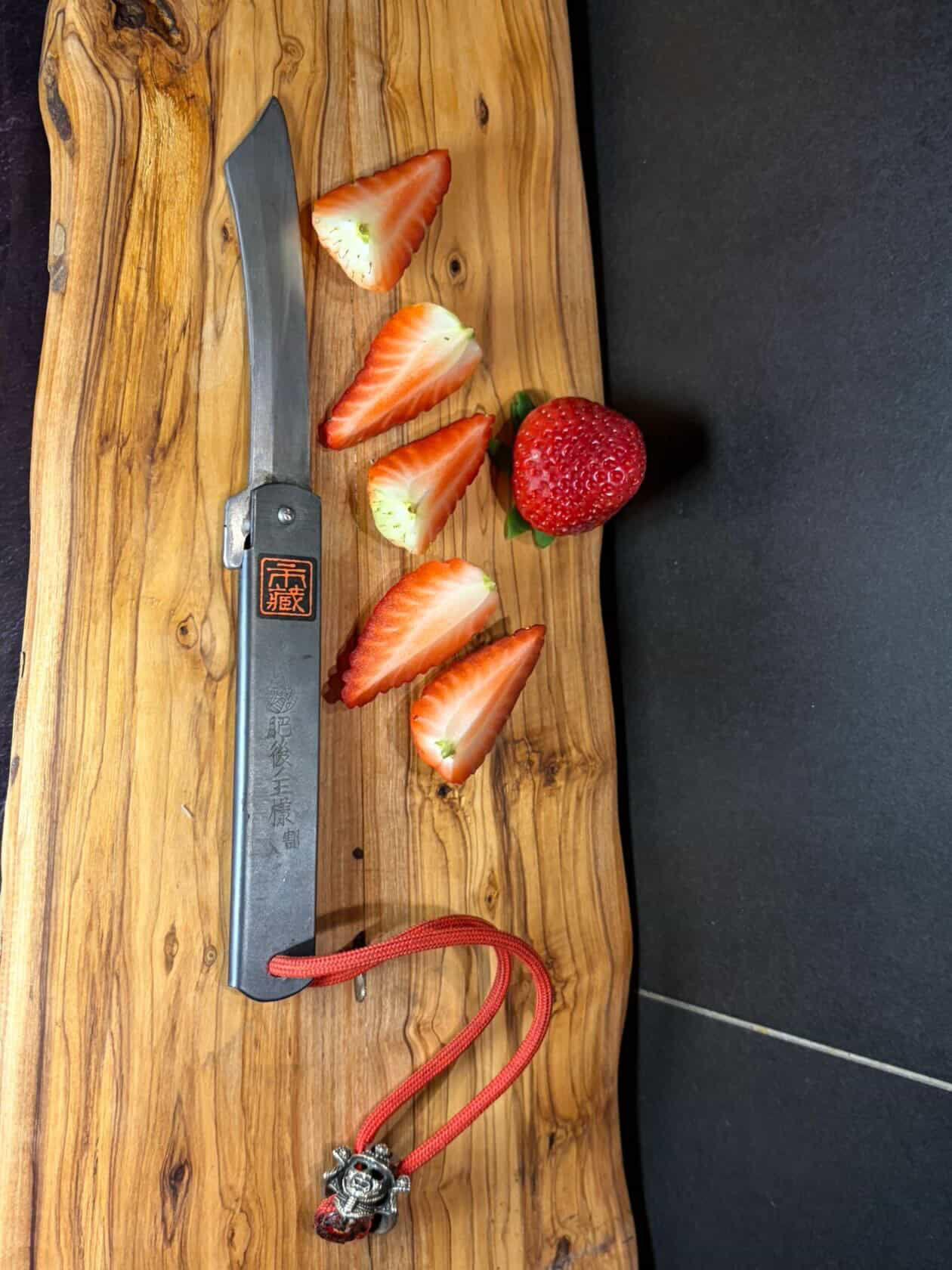 Ichizo Honpo Higonokami pocket knife with freshly cut strawberries on olive wood board