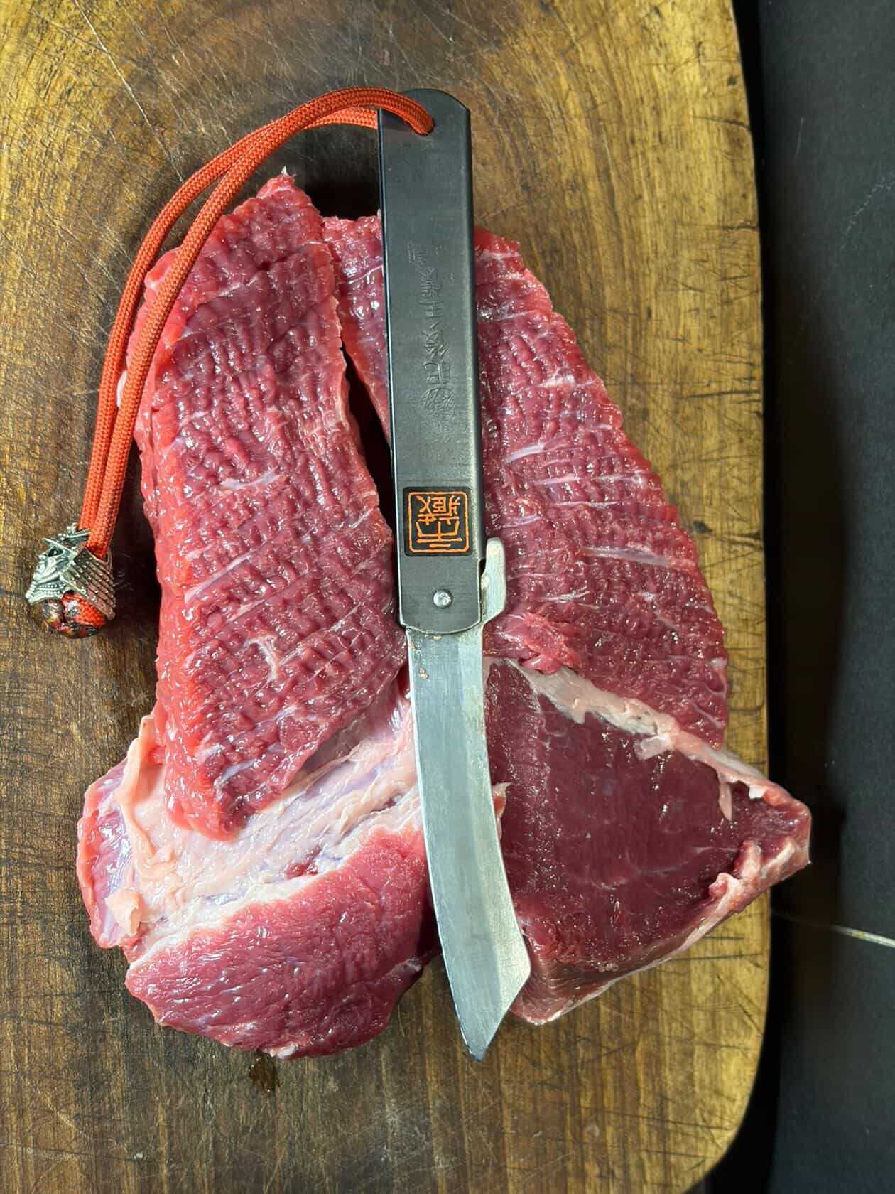 Ichizo Honpo Higonokami knife cutting through raw beef on wooden board