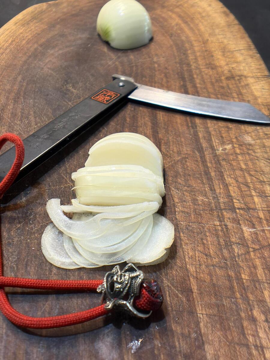 Thinly sliced onion beside an open Ichizo Honpo Higonokami