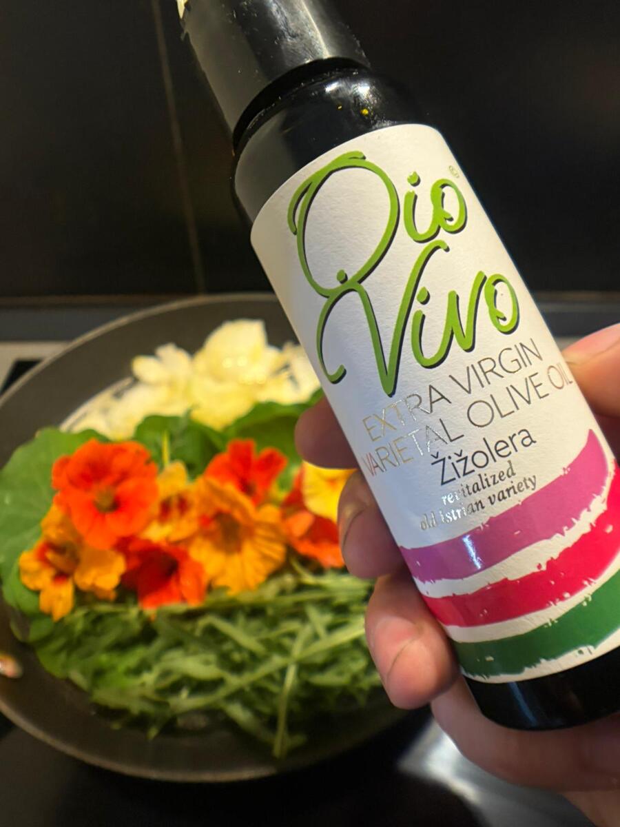 Bottle of Istrian olive oil beside a pan filled with nasturtium flowers, wild greens, and onion