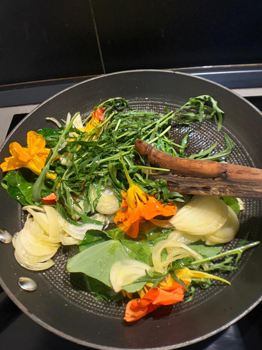 Nasturtium flowers, wild greens, and onion cooking together in a pan