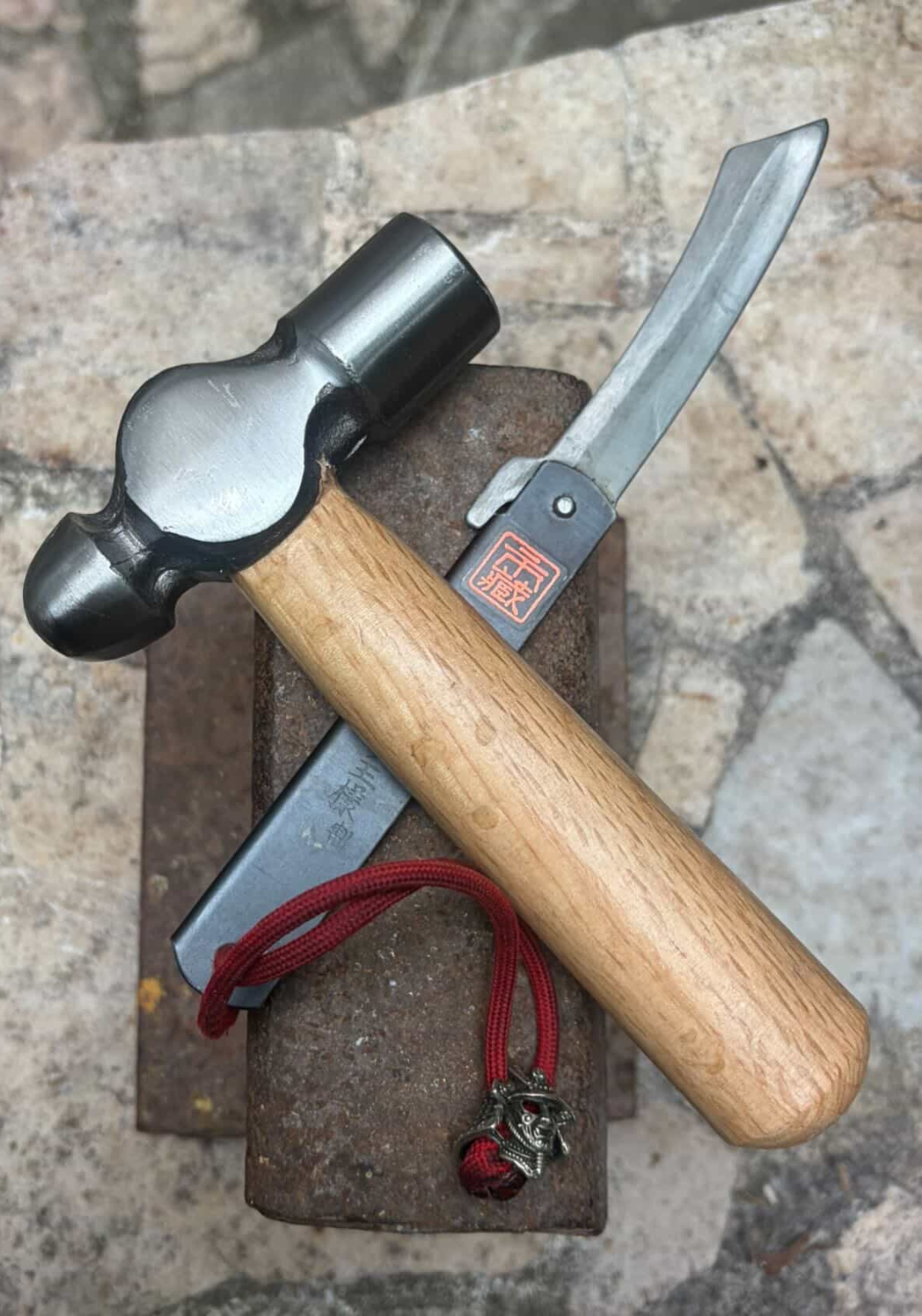 A Higonokami resting on a piece of railway rail alongside a small hammer