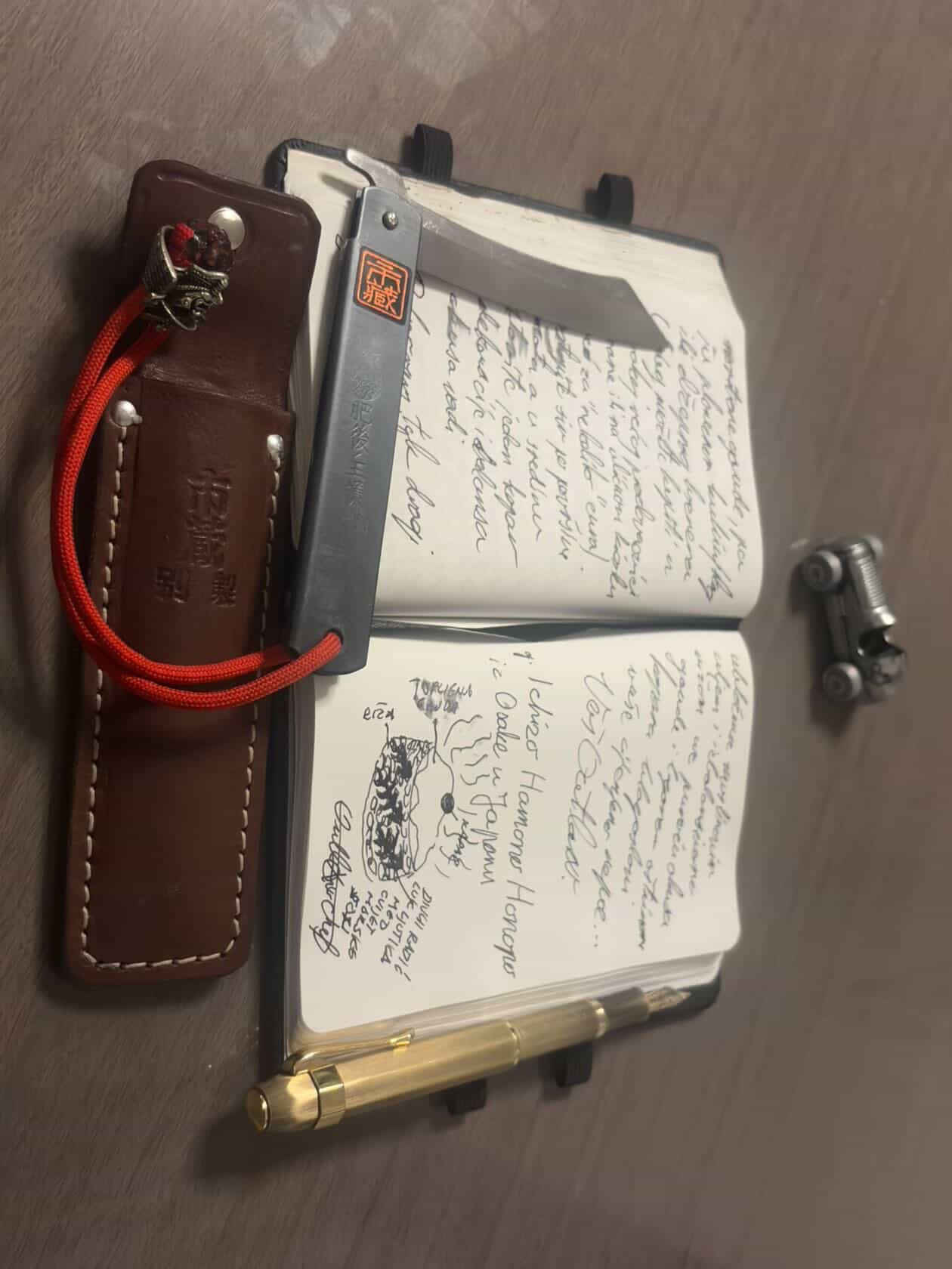 Outlaw Chef's notebook with 'Ichizo Hamono Honopo' written in his hand, with the Higonokami in its leather case beside it