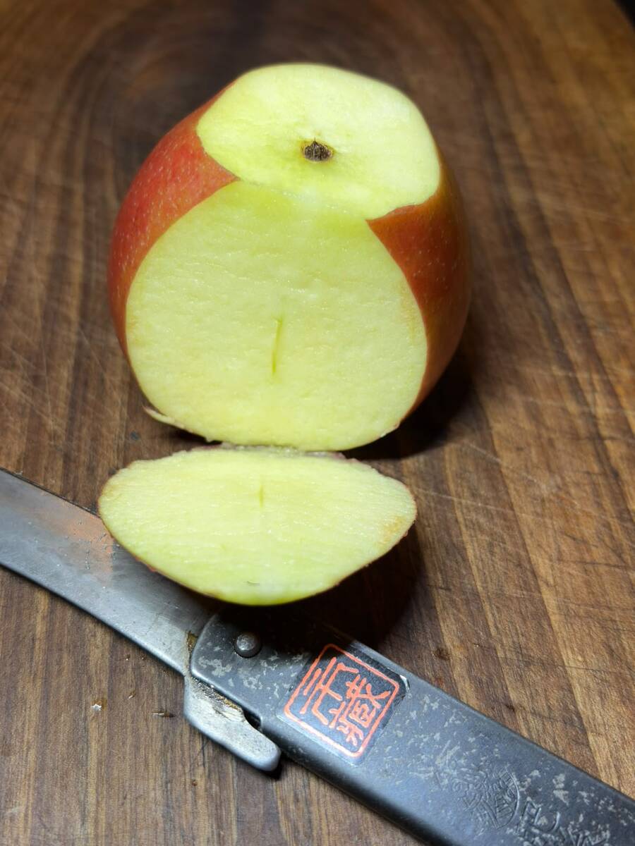A sliced apple and an Ichizo Honpo Higonokami on a wooden cutting board