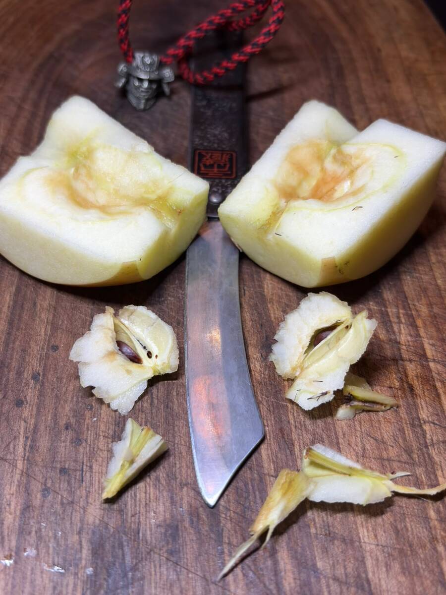 Two cored apple halves with an Ichizo Honpo Higonokami between them, with its red cord and samurai charm