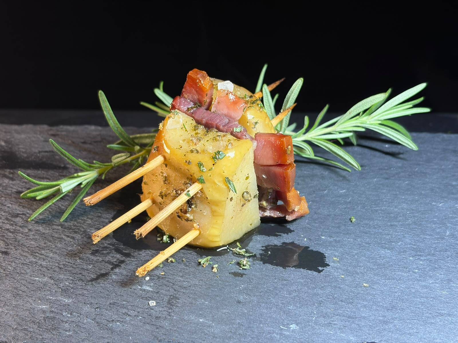 The baked apple, pinned with skewers, on a slate board with sprigs of rosemary