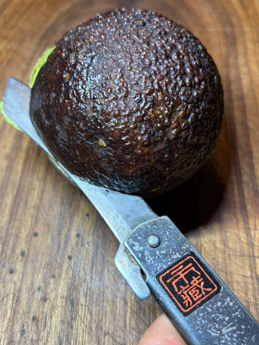 A whole avocado and a Higonokami bearing the Ichizo stamp on a wooden cutting board
